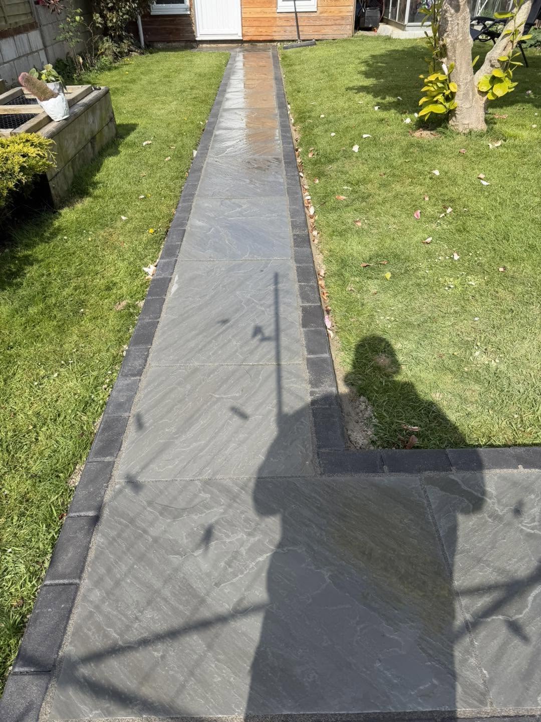 A grey paved path across the lawn with a charcoal edge