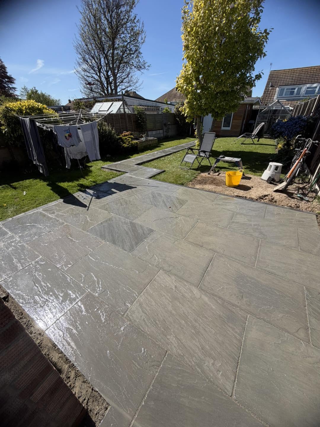A grey paved patio with a lawn and trees beyond