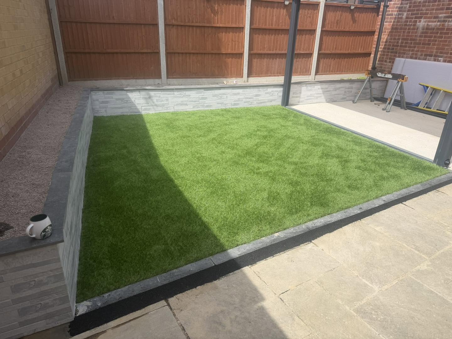Artificial grass with a raised block edge beside a light paved patio