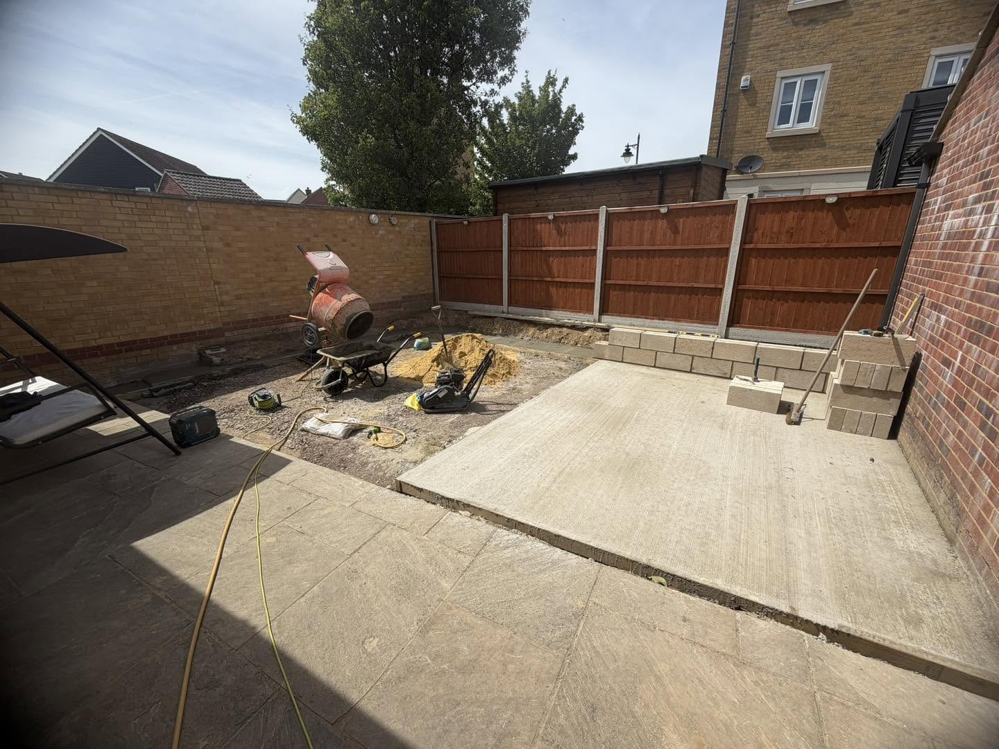 A fresh concrete base laid in a walled back garden, with a cement mixer behind