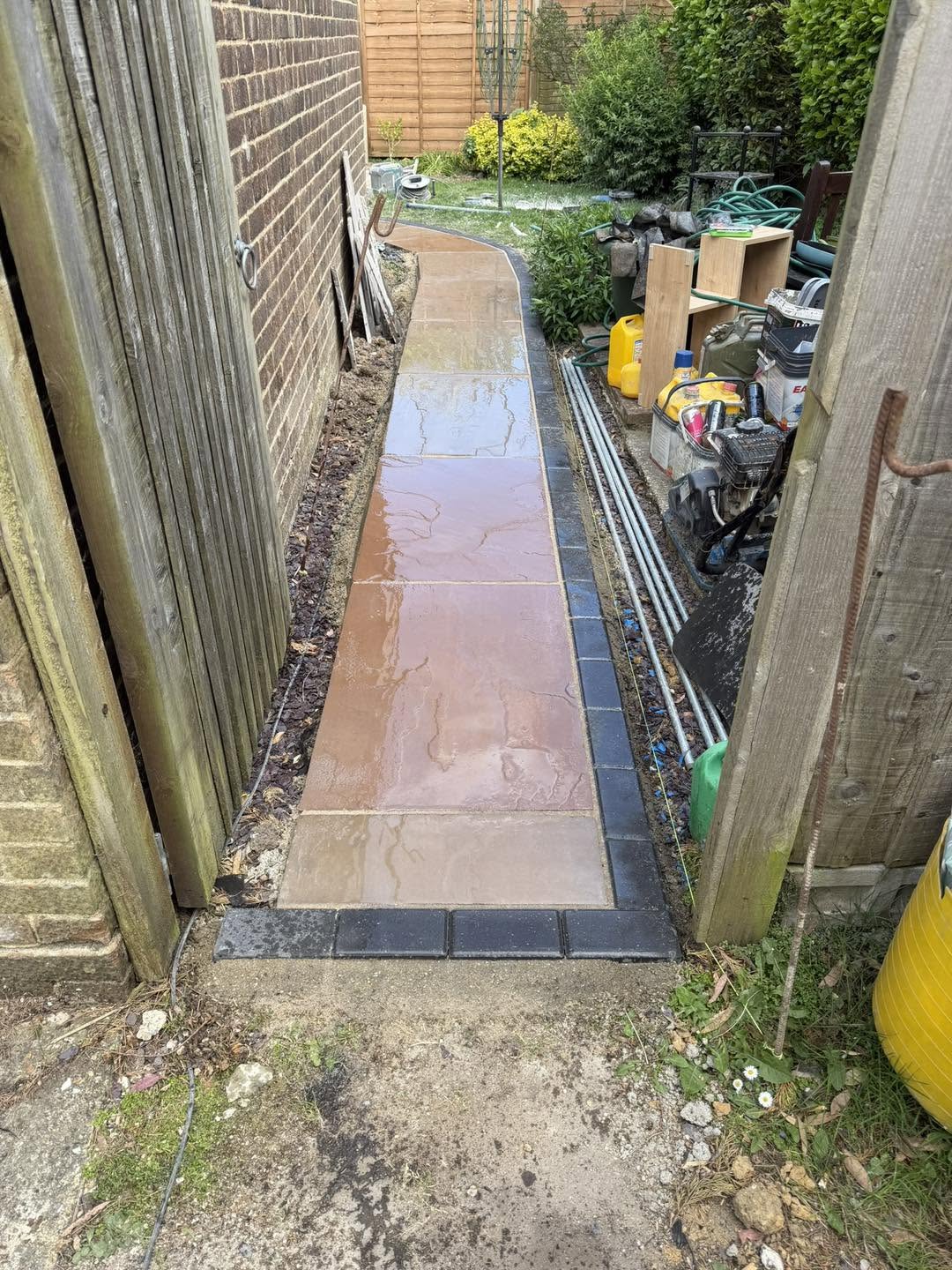 A paved path running down the side of the house with a dark block edge