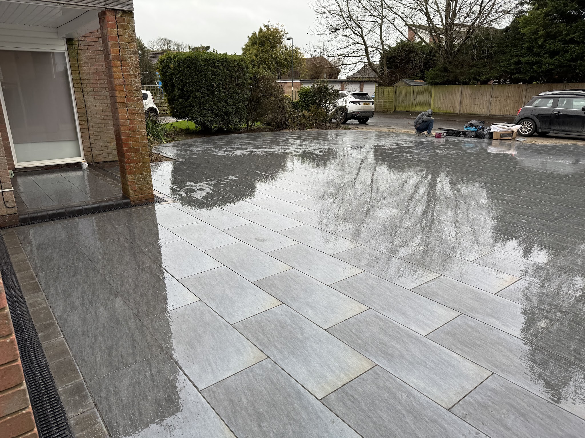 A large-format light grey porcelain patio with a drainage channel along the house