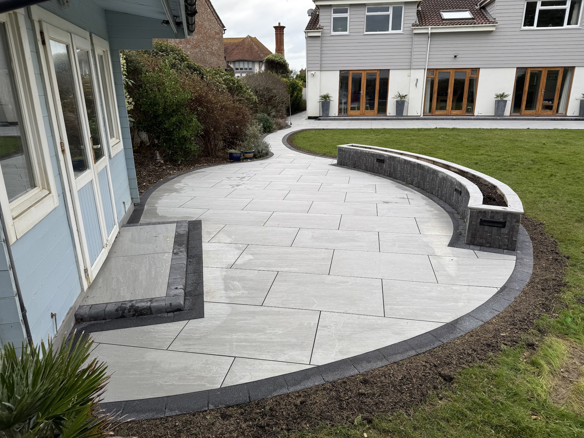 A curved light grey porcelain patio with a curved dark block wall, laid by DS Driveways & Patios